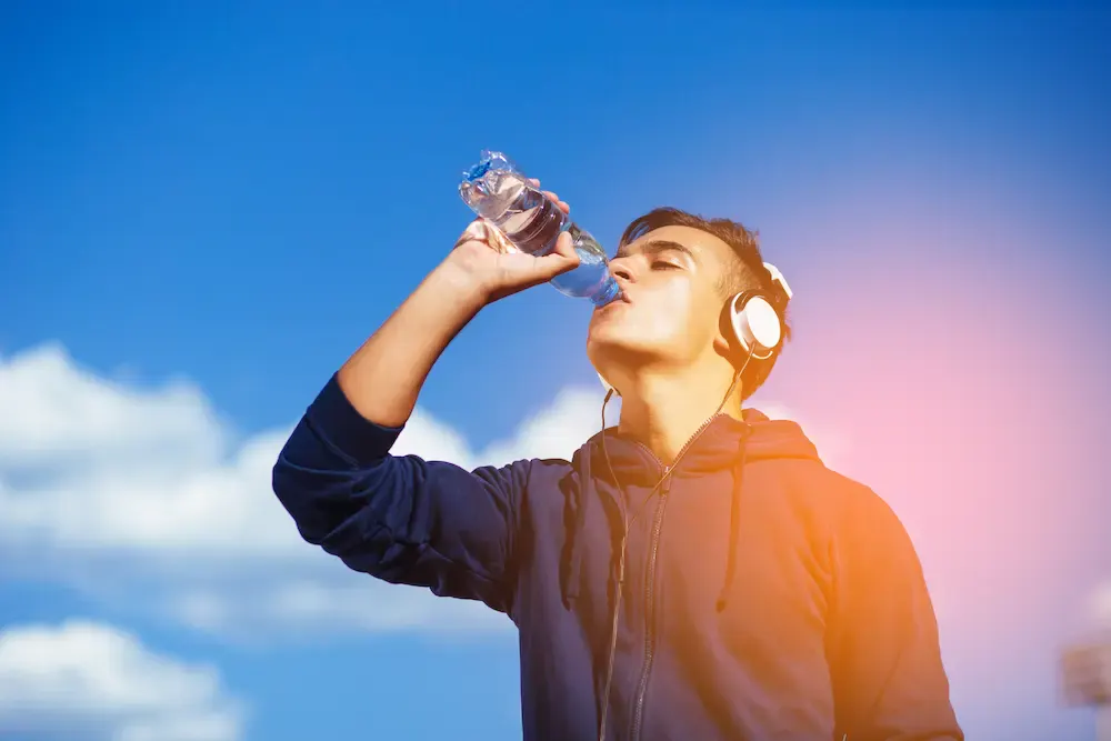 A young male athlete drinking water outdoors from a plastic bottle to stay hydrated.