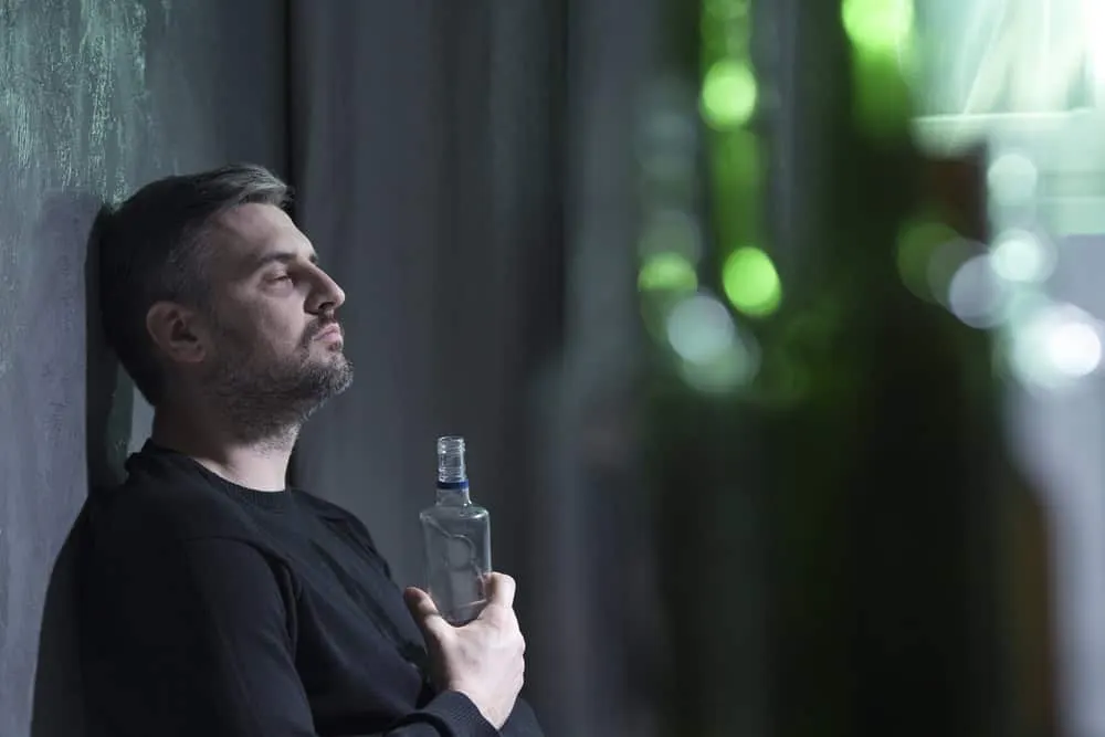 Man with dark circles holding a bottle highlighting the challenges of maintaining sobriety and the public perception during the recovery journey