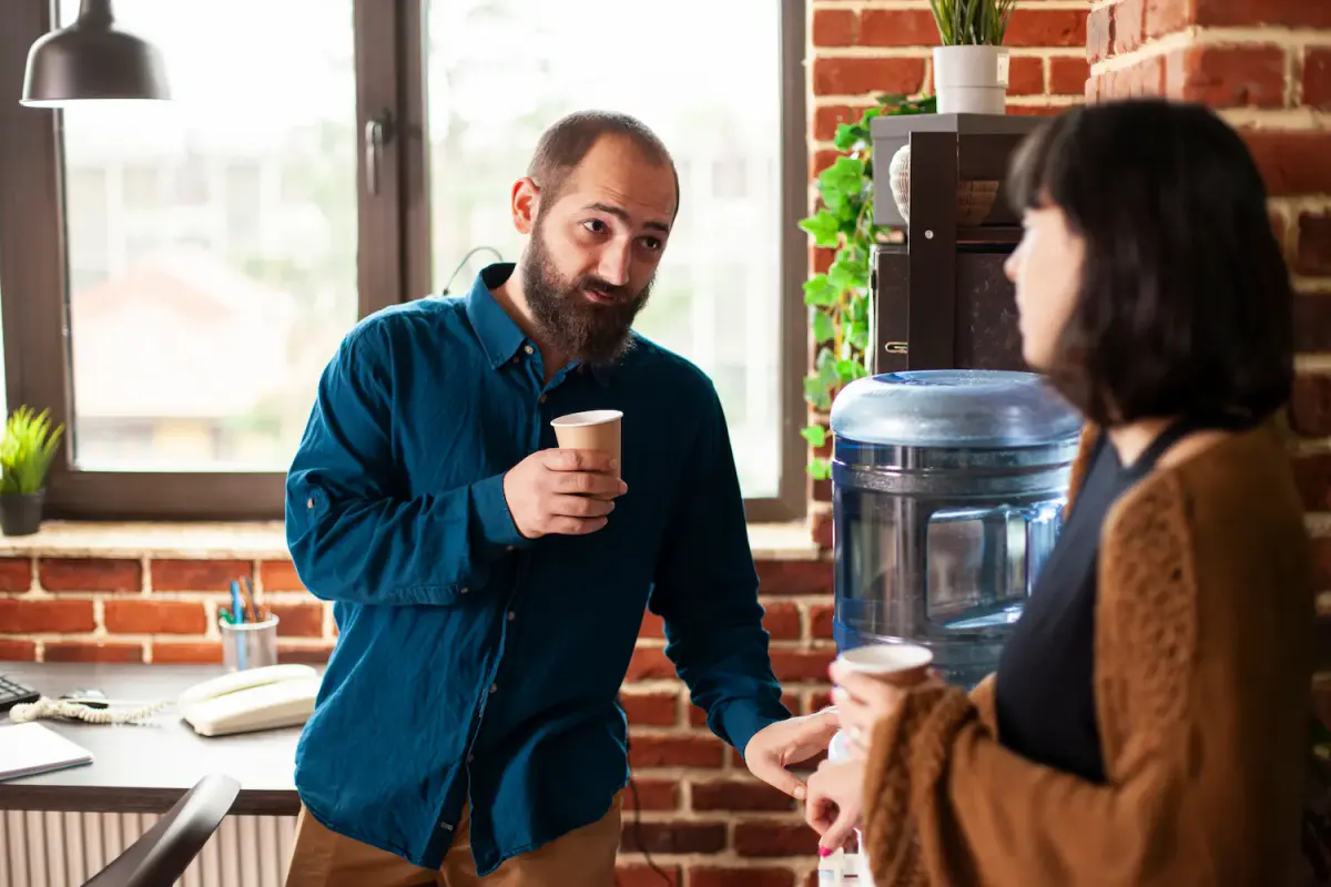 Two colleagues chatting casually by an office water cooler, illustrating how Texas employers can foster a supportive and ordinary workplace environment for individuals returning from addiction treatment.