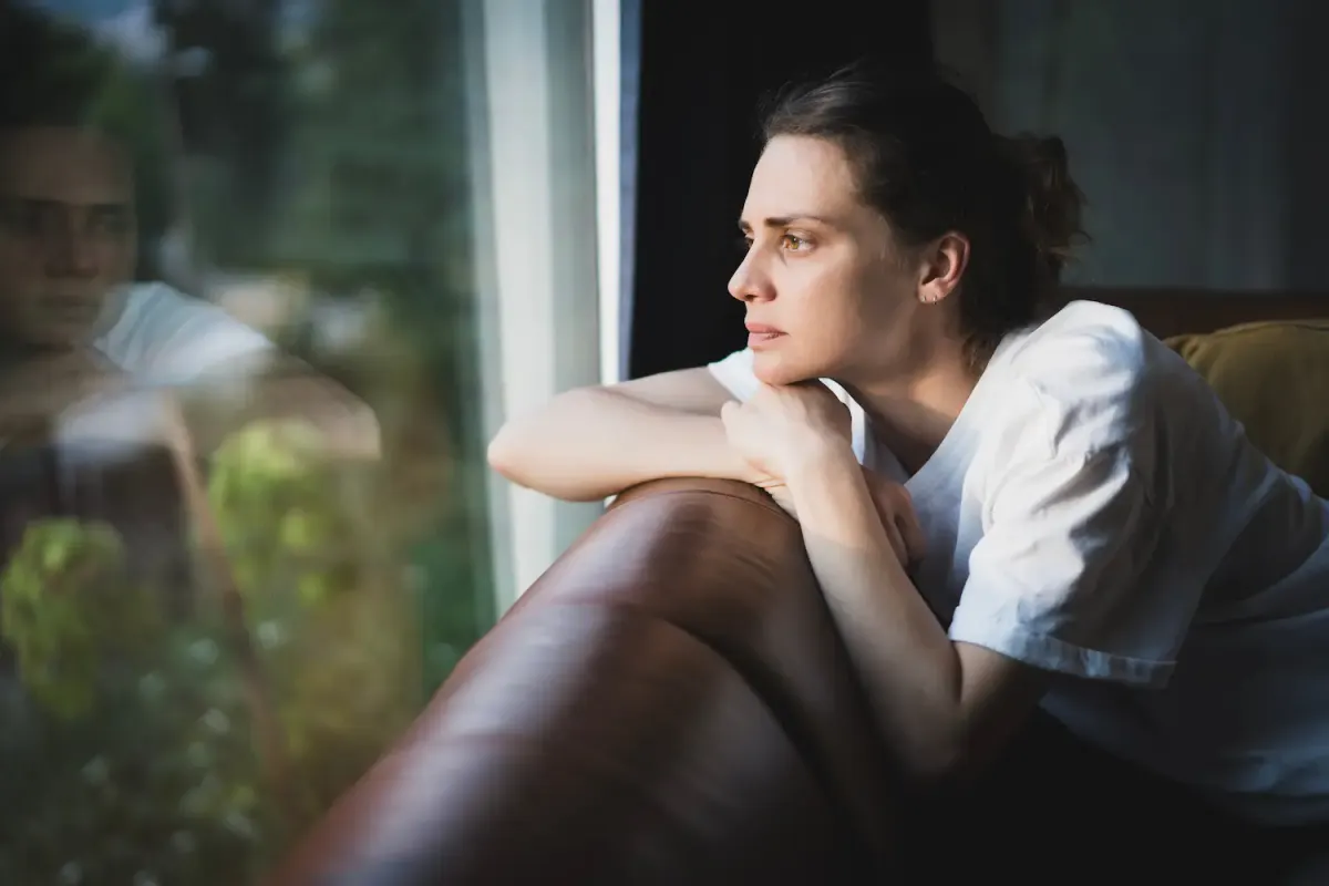 A pensive woman gazing out a window while resting on a couch, illustrating the quiet emotional distress, depression, and isolation that can accompany co-occurring substance use and mental health conditions.